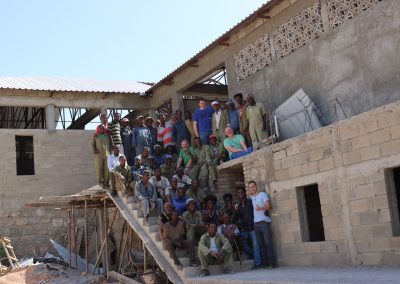 Ein deutsches Handwerkerteam sitzt mit seinen eritreischen Kollegen auf der Treppe des Neubaus der Mutter-Kind-Klinik in Keren, Eritrea